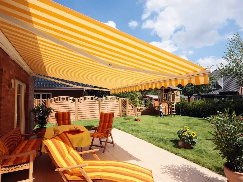 Eine sonnige Terrasse mit einer gestreiften Markise, die Schatten spendet, ausgestattet mit Holzstühlen und einem Tisch.