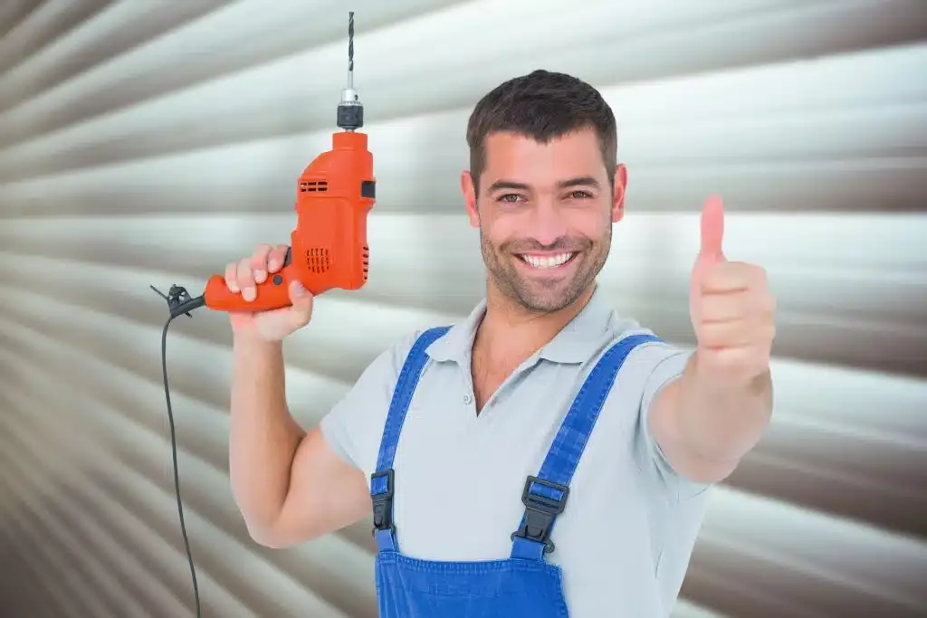 Handwerker im Overall hält eine Bohrmaschine in der Hand und streckt den Daumen nach oben.