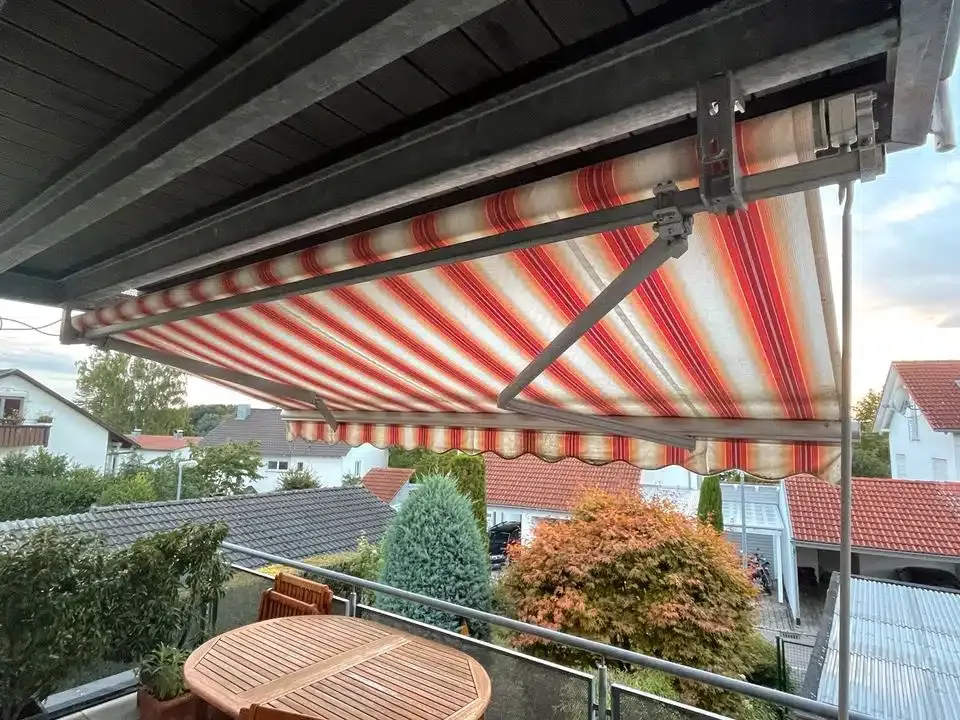 Ausziehbare Markise, die sich über einen Wohnbalkon mit Gartenmöbeln erstreckt und Schatten und Ausblick auf die Nachbarhäuser bietet.