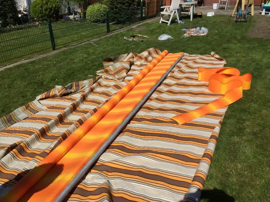 Ein ausgebreiteter orange-weiß gestreifter Zeltstoff liegt auf dem Gras, daneben sind Stangen, wahrscheinlich wird er gerade auf- oder abgebaut.