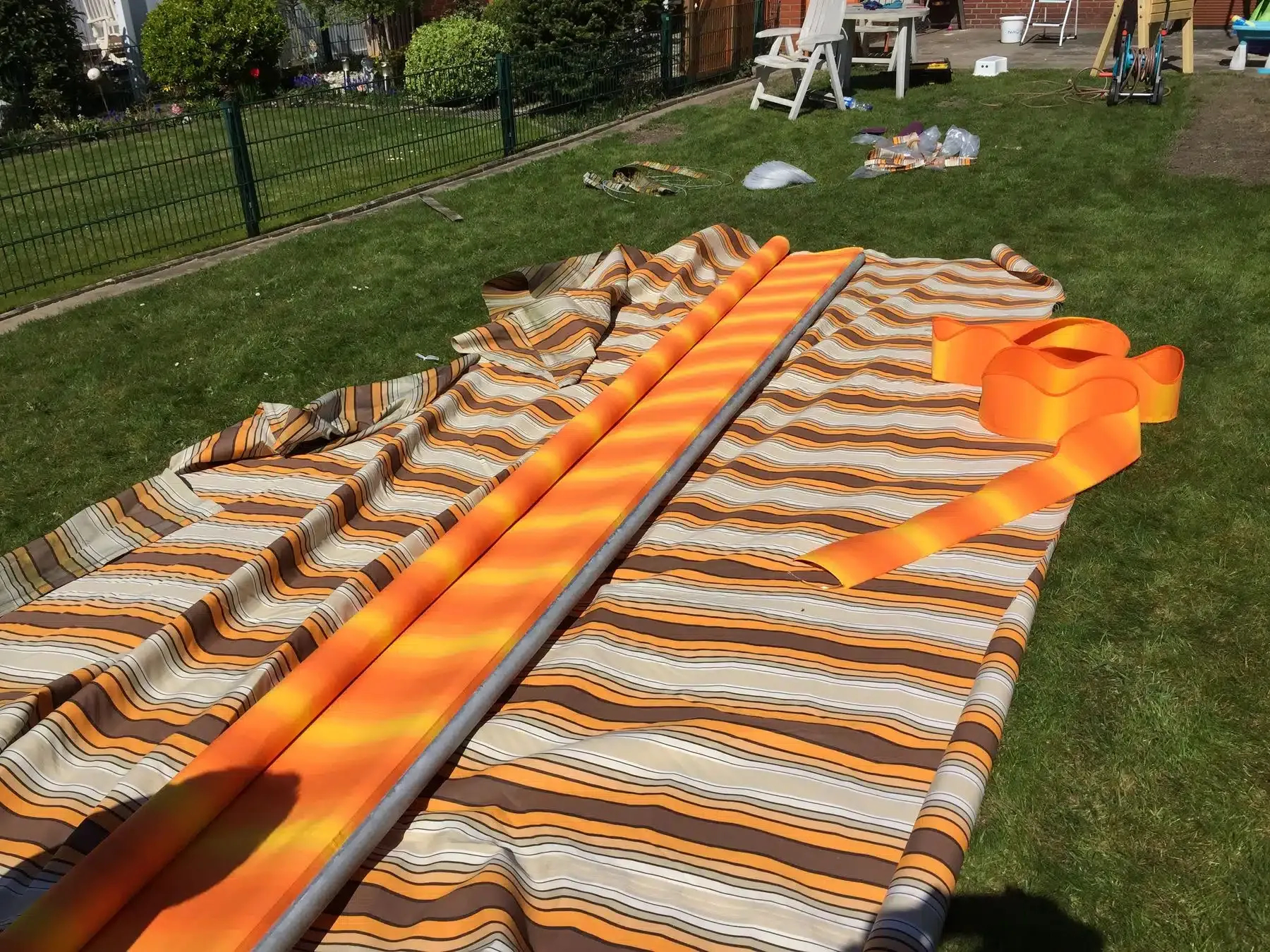 Ein ausgebreiteter orange-weiß gestreifter Zeltstoff liegt auf dem Gras, daneben sind Stangen, wahrscheinlich wird er gerade auf- oder abgebaut.