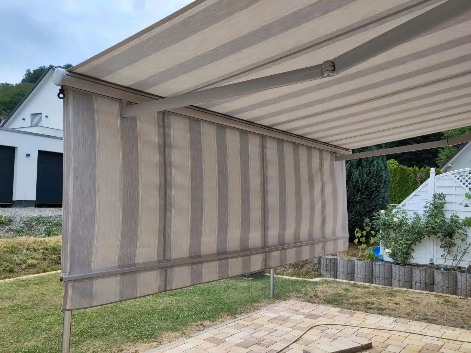 Eine gestreifte Markise mit Seitenmarkise, die sich über einen Terrassenbereich erstreckt.